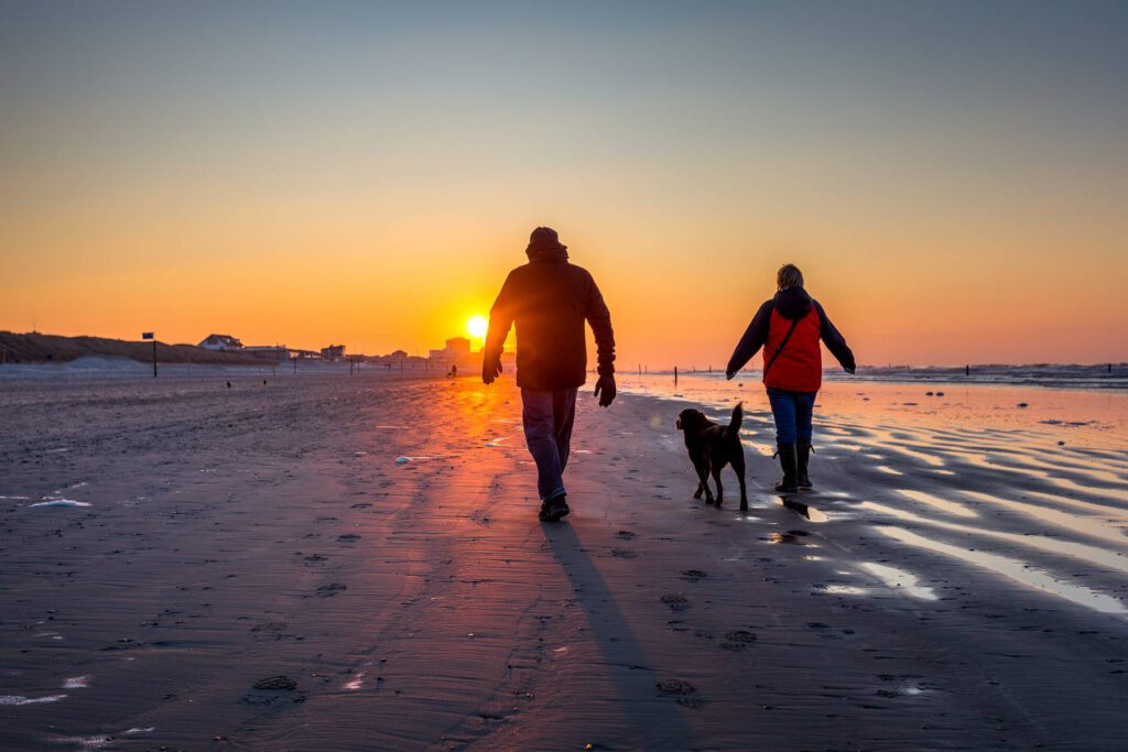 Winterspaziergang mit Hund am Strand von Norderney bei Sonnenuntergang